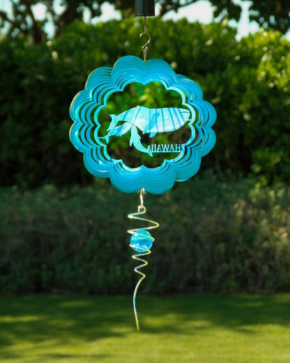 Decorative wind spinner with blue whale family design and 'Hawaii' text against a green outdoor background.